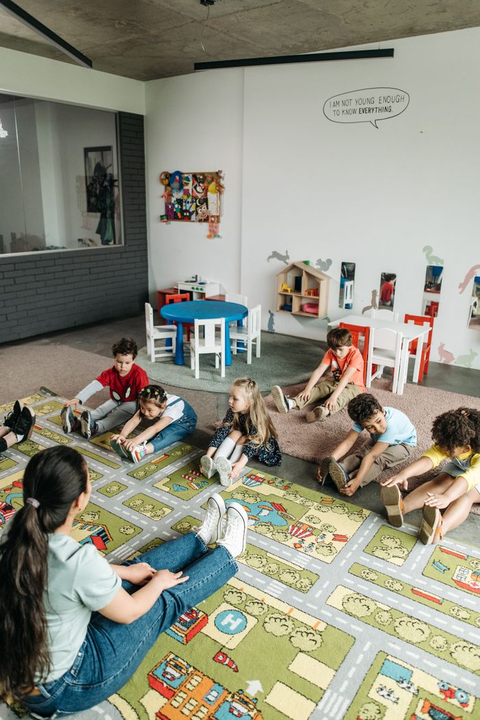 Kindergarten children participating in a classroom exercise on a colorful mat.