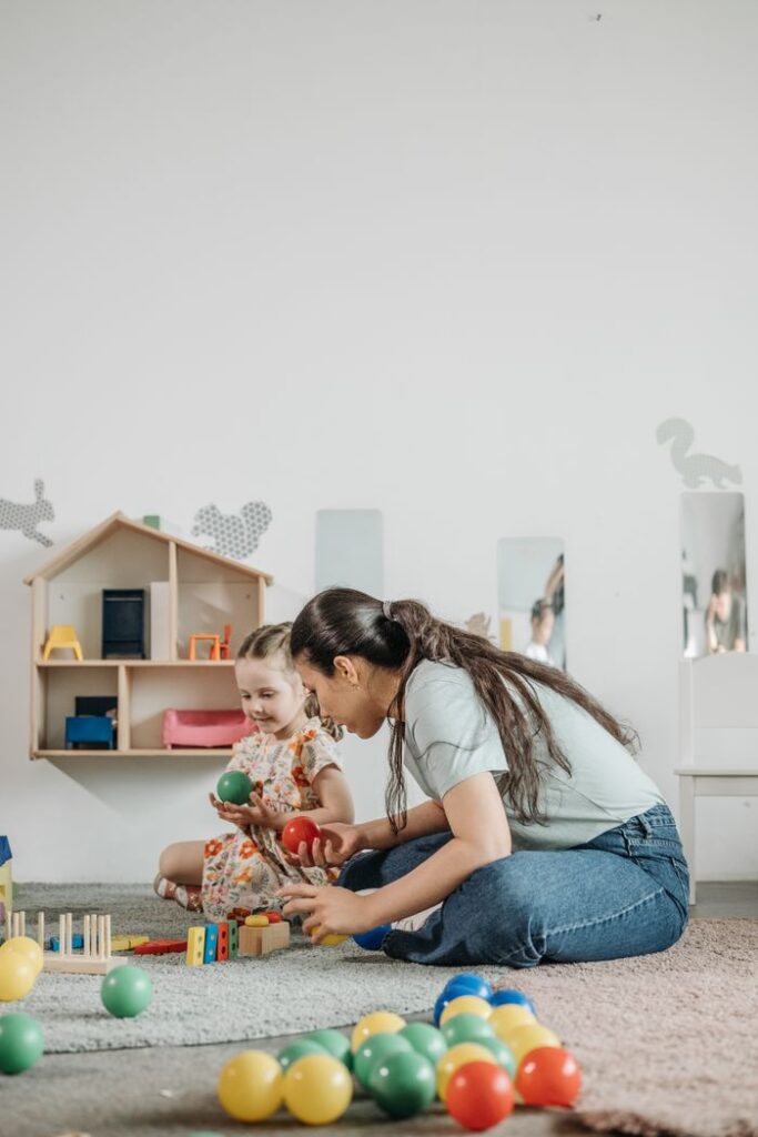 A child and educator engage in playful learning with toys in a kindergarten classroom.