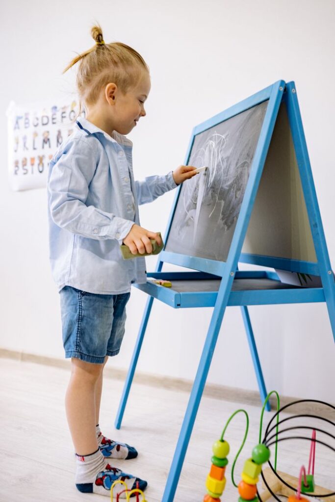 A young child writing on a blackboard in a bright classroom setting, focusing on early education.